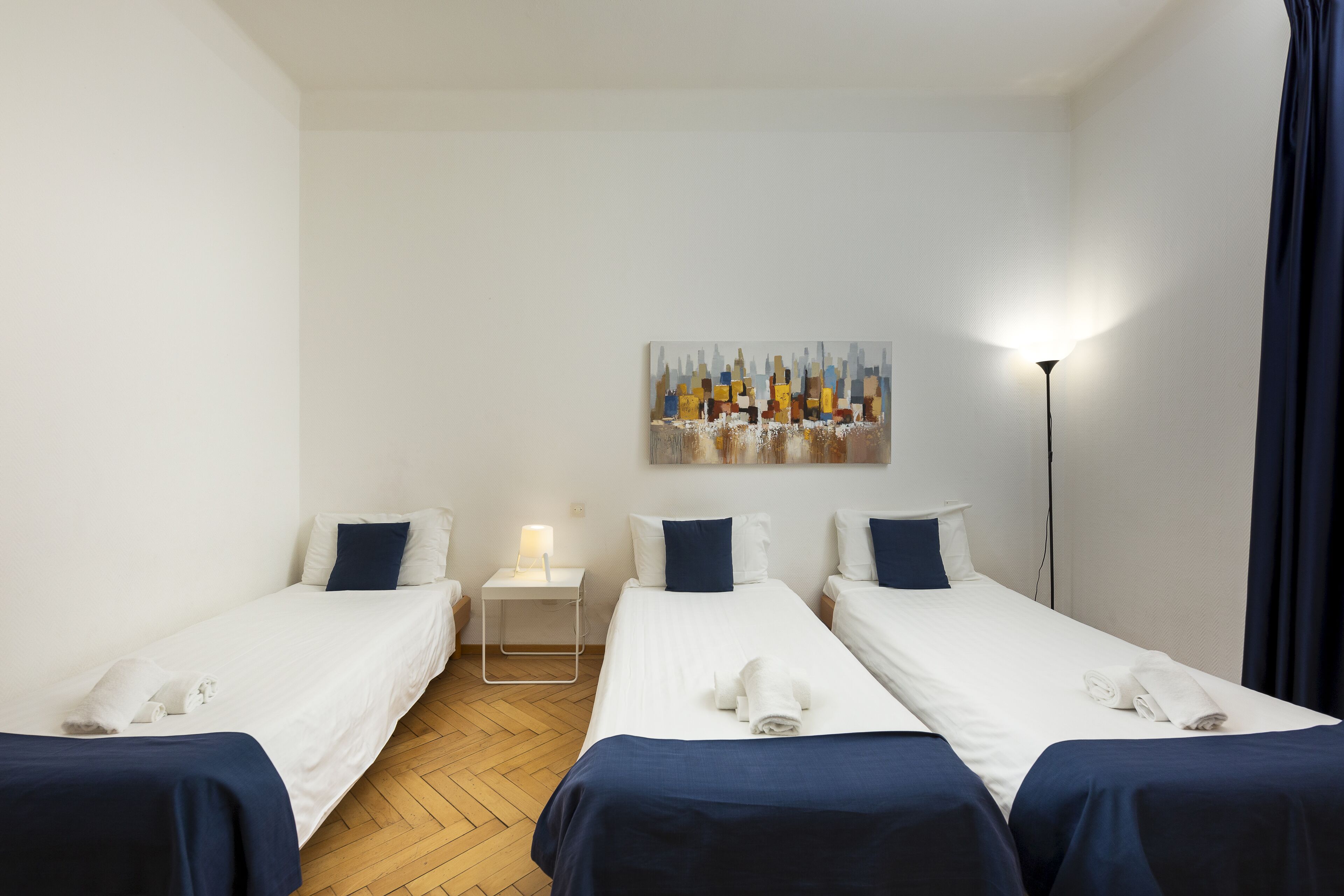 Ein Hotelzimmer mit zwei Einzelbetten, einem kleinen Nachttisch mit Lampe, einem Bild an der Wand und einer Stehlampe.