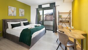 A hotel room with a bed, a dining table, a chair, and a balcony with a view of buildings. - Lugano Center GuestHouse (Lugano)