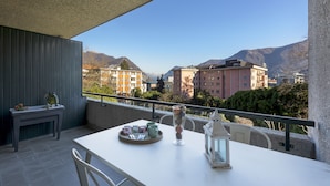 A balcony with a table, chairs, and a view of buildings and mountains. - Lugano Center GuestHouse (Lugano)