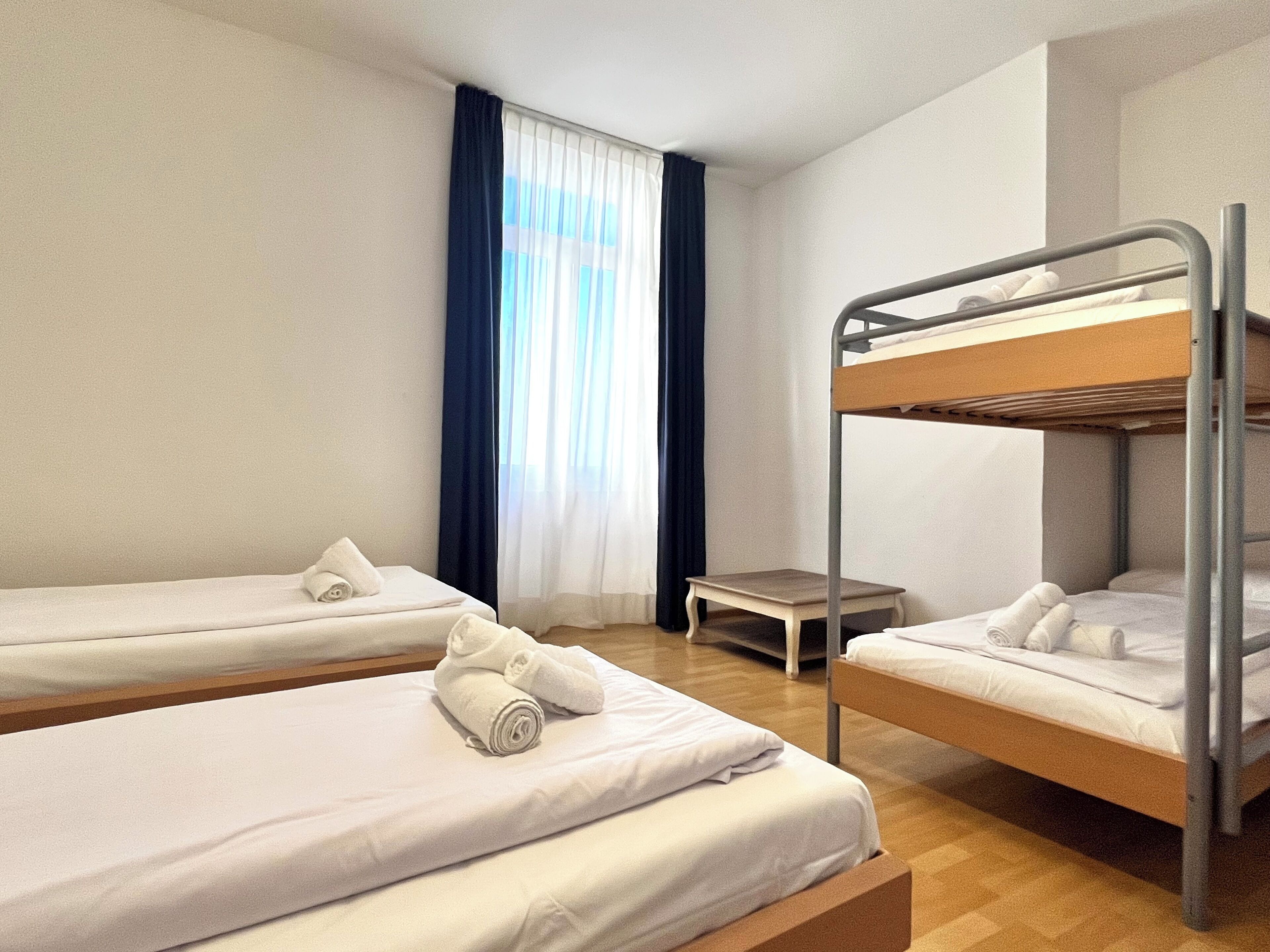 A room with two bunk beds, a small table, and a window with curtains.