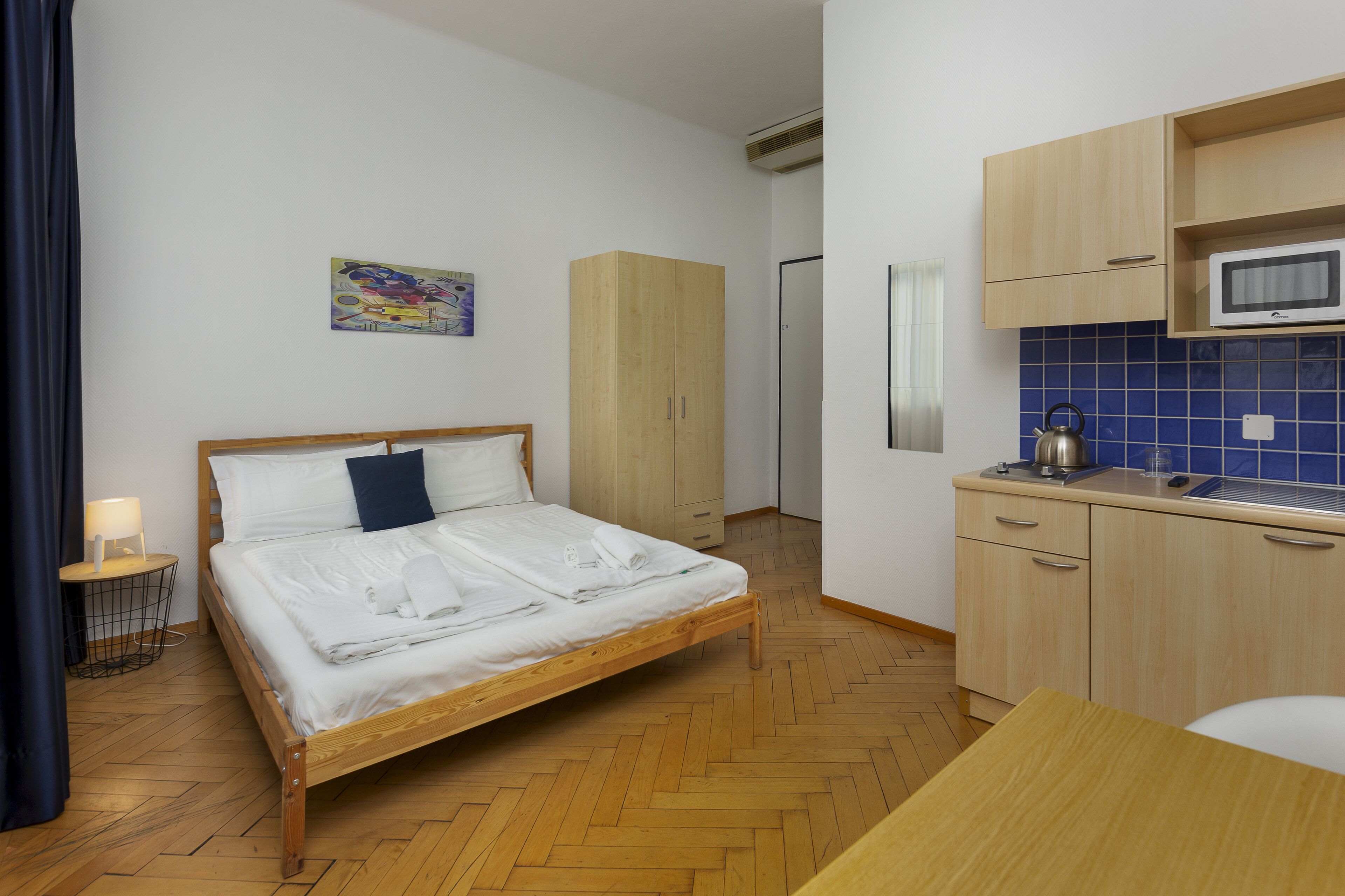 Ein Schlafzimmer mit einem hölzernen Bett, einem Nachttisch, einem Kleiderschrank und einer Küchenzeile mit einer Mikrowelle.
