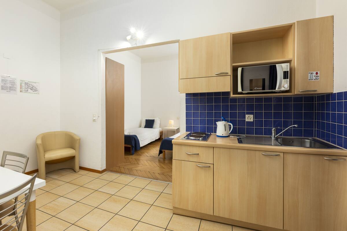 A compact kitchen with a microwave, sink, and a small dining area with a chair and table.