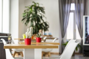 Ruokailutila, jossa on puinen pöytä ja valkoiset tuolit. Taustalla on ruukussa oleva kaktus ja suuri kasvi.