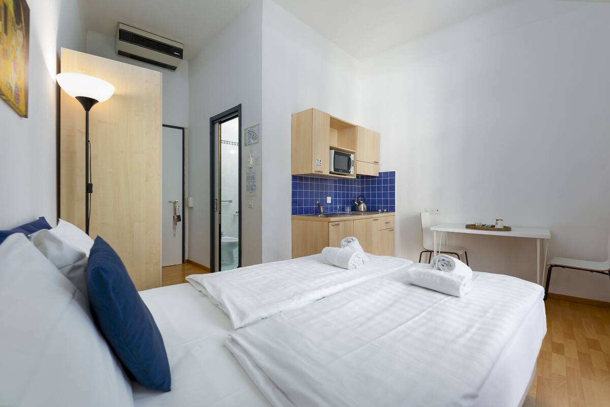 A hotel room with a bed, a desk, a microwave, and a small kitchenette.