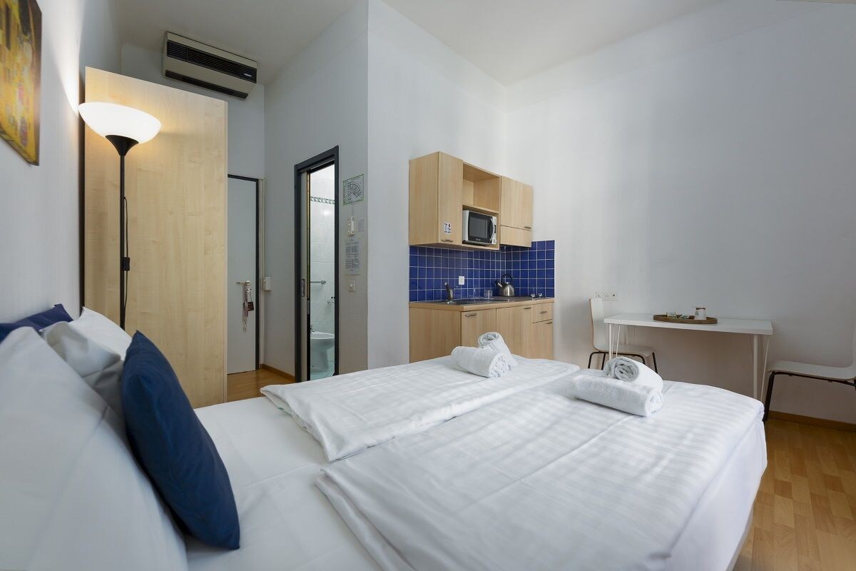 A hotel room with a bed, a desk, a kitchenette, and a bathroom.