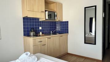 Una habitación de hotel compacta con cama, kitchenette con microondas y un espejo.