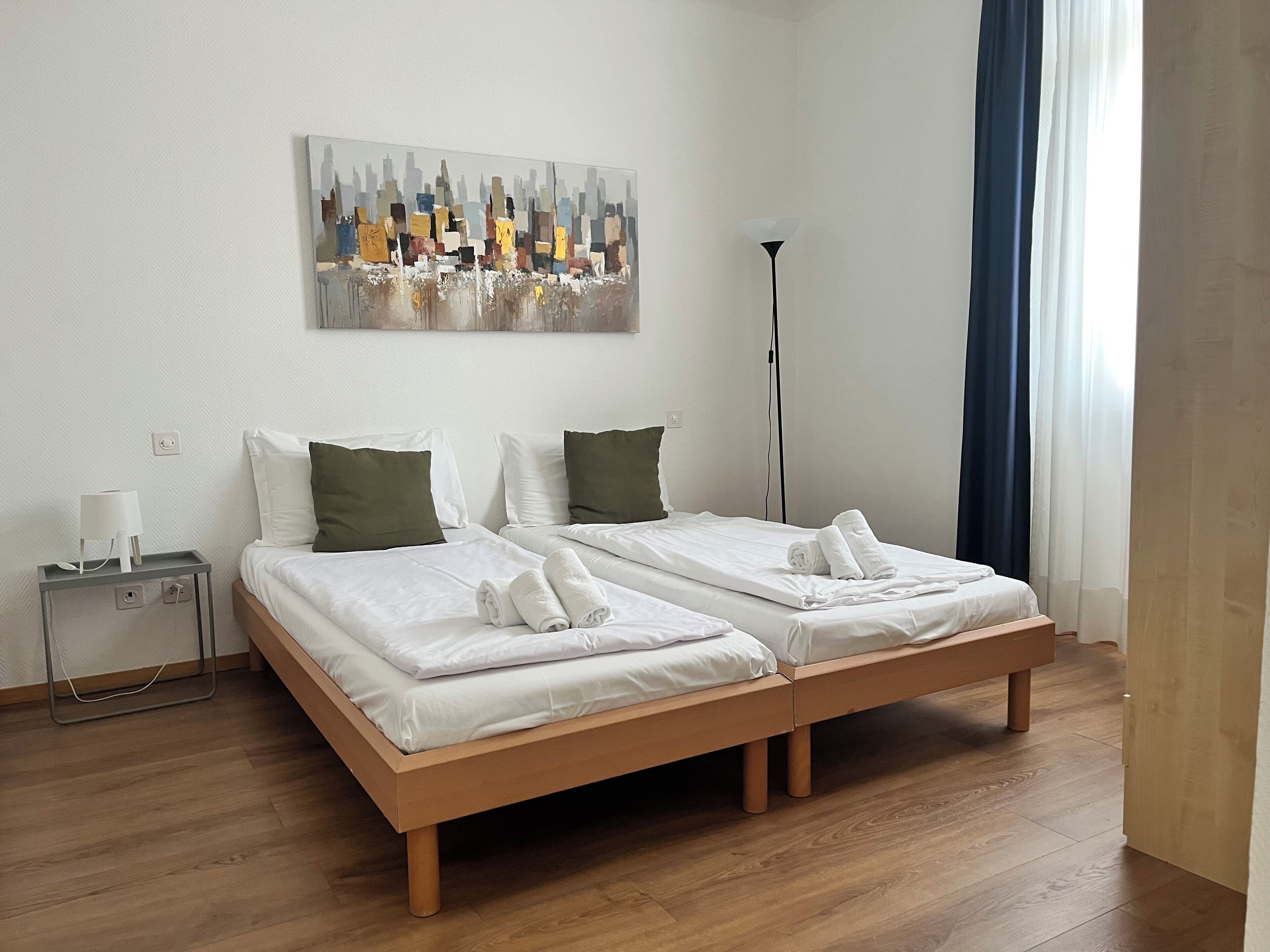 Una habitación de hotel con dos camas, una mesita de noche, una lámpara y un cuadro en la pared.
