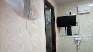 A bathroom with a patterned wallpaper, a fan, a shower, a mirror, and a mounted TV. - Mabuhay Hotel (Kowloon)