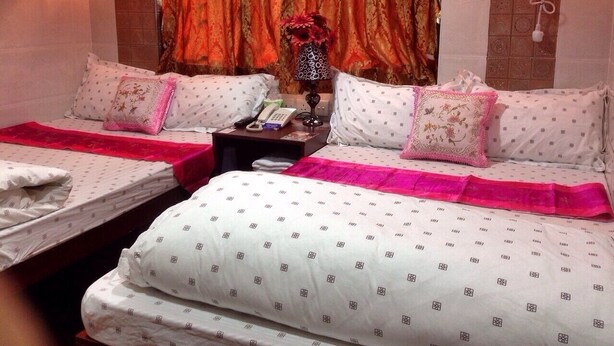 A hotel room with two beds, each with a pink bedspread, a nightstand with a telephone and a vase with flowers, and a curtain with a red and gold pattern. - Mabuhay Hotel (Kowloon)