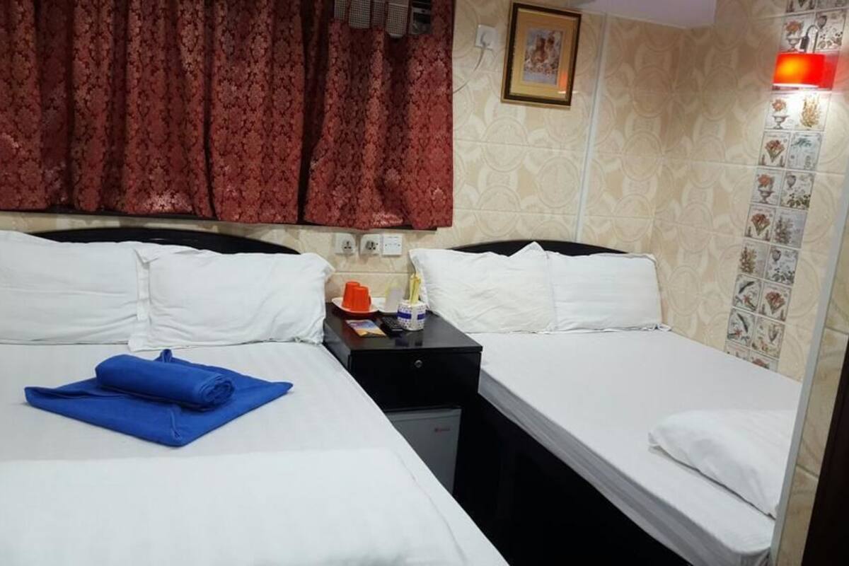 Une chambre d’hôtel avec deux lits, une table de chevet, un rideau rouge, un lampadaire fixé au mur et un petit réfrigérateur.