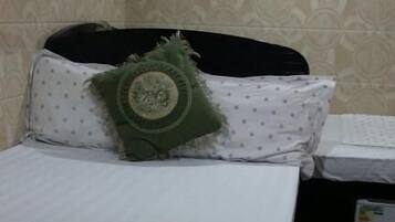 A bed with a white bedspread and a green pillow, a small table with a white cloth, and a wall-mounted air conditioner.