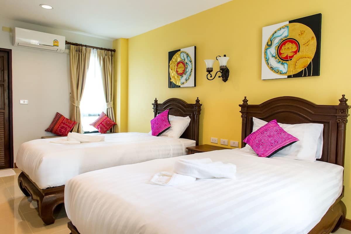Ein Hotelzimmer mit zwei Betten, jeweils mit weißer Bettwäsche und dekorativen Kissen. Über jedem Bett befinden sich Wandlampen und ein Gemälde.