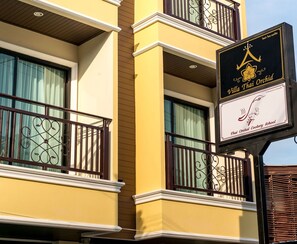 A building with a sign for Villa Thai Orchid, featuring balconies with wrought iron railings and a Thai Orchid Cookery School logo.