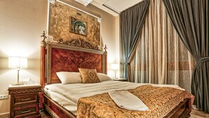 A large bed with a wooden headboard, a bedside table with a lamp, and a curtain on the window. - Arbia Dorka Heritage Palace (Varazdin)