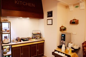 Zona de cocina de hotel con un bufé, que incluye una máquina de café, un tostador y diversos alimentos a la vista.