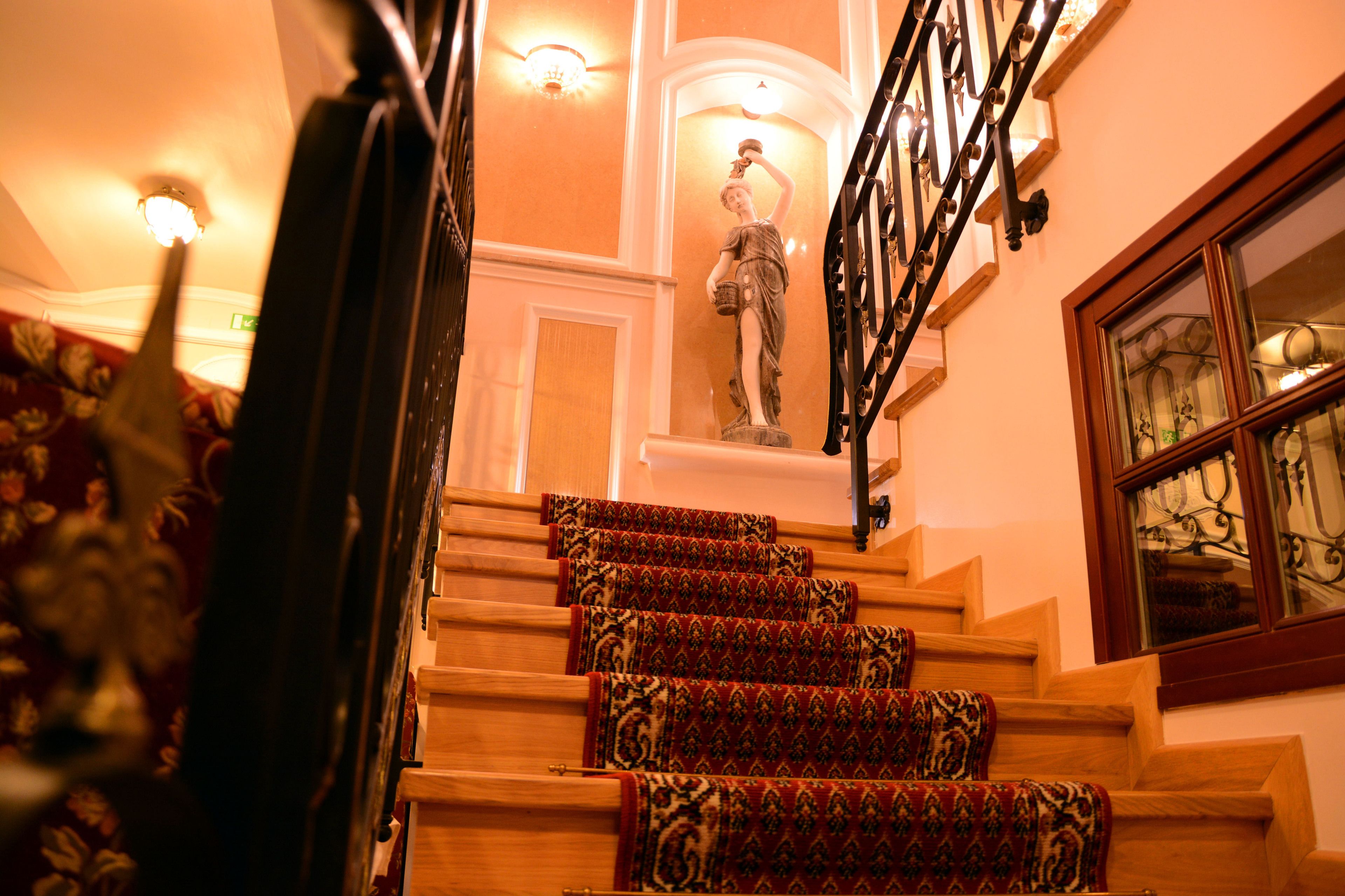 A staircase with ornate carpeted steps, a statue, and a wrought iron railing.