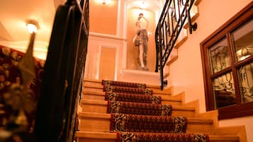 A staircase with ornate carpeted steps, a statue, and a wrought iron railing.