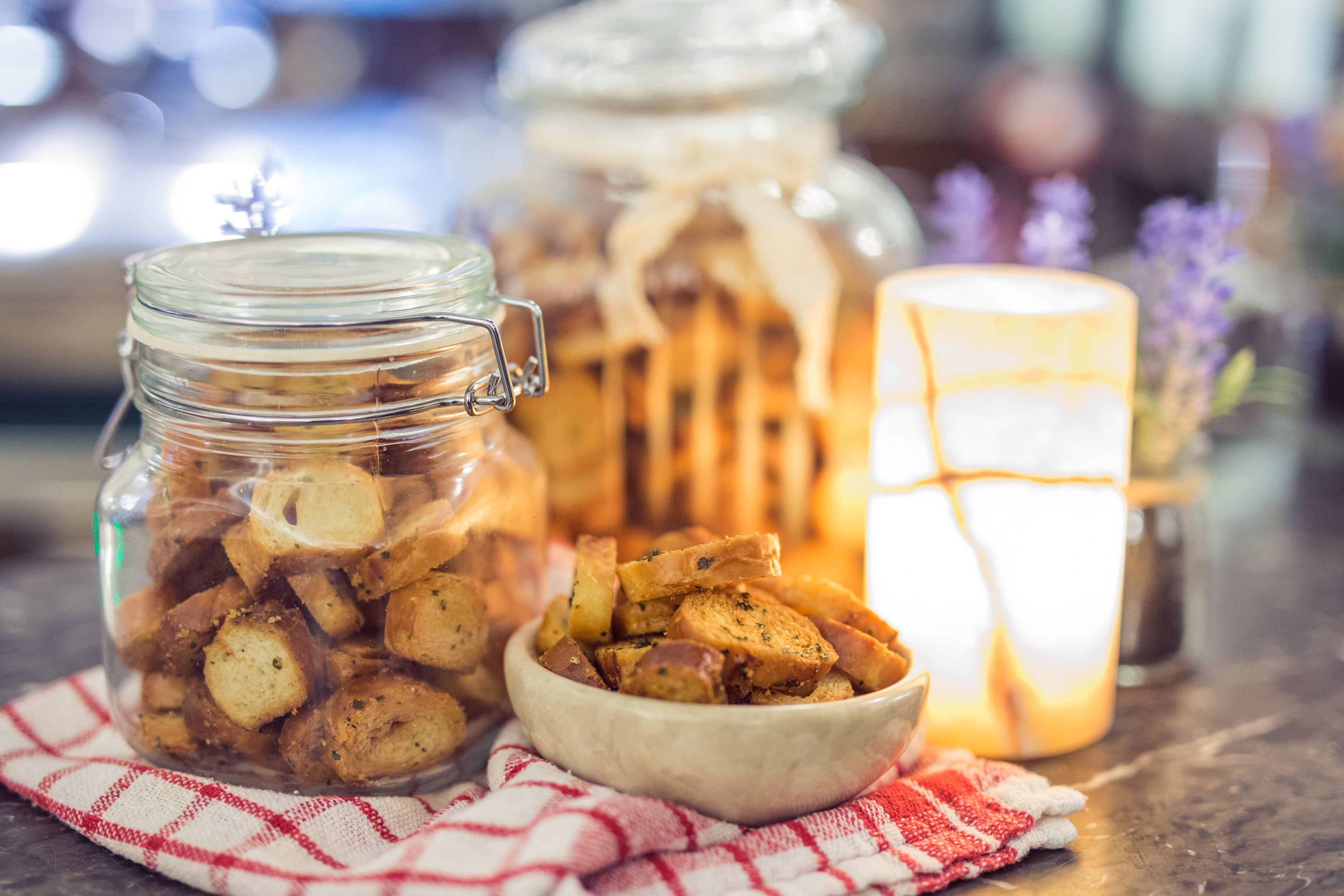A jar filled with food items, a bowl of food, and a lit candle on a table.