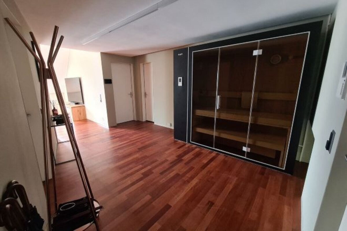 A spacious room with a wooden floor, a large wardrobe with sliding doors, and a ladder leaning against the wall.