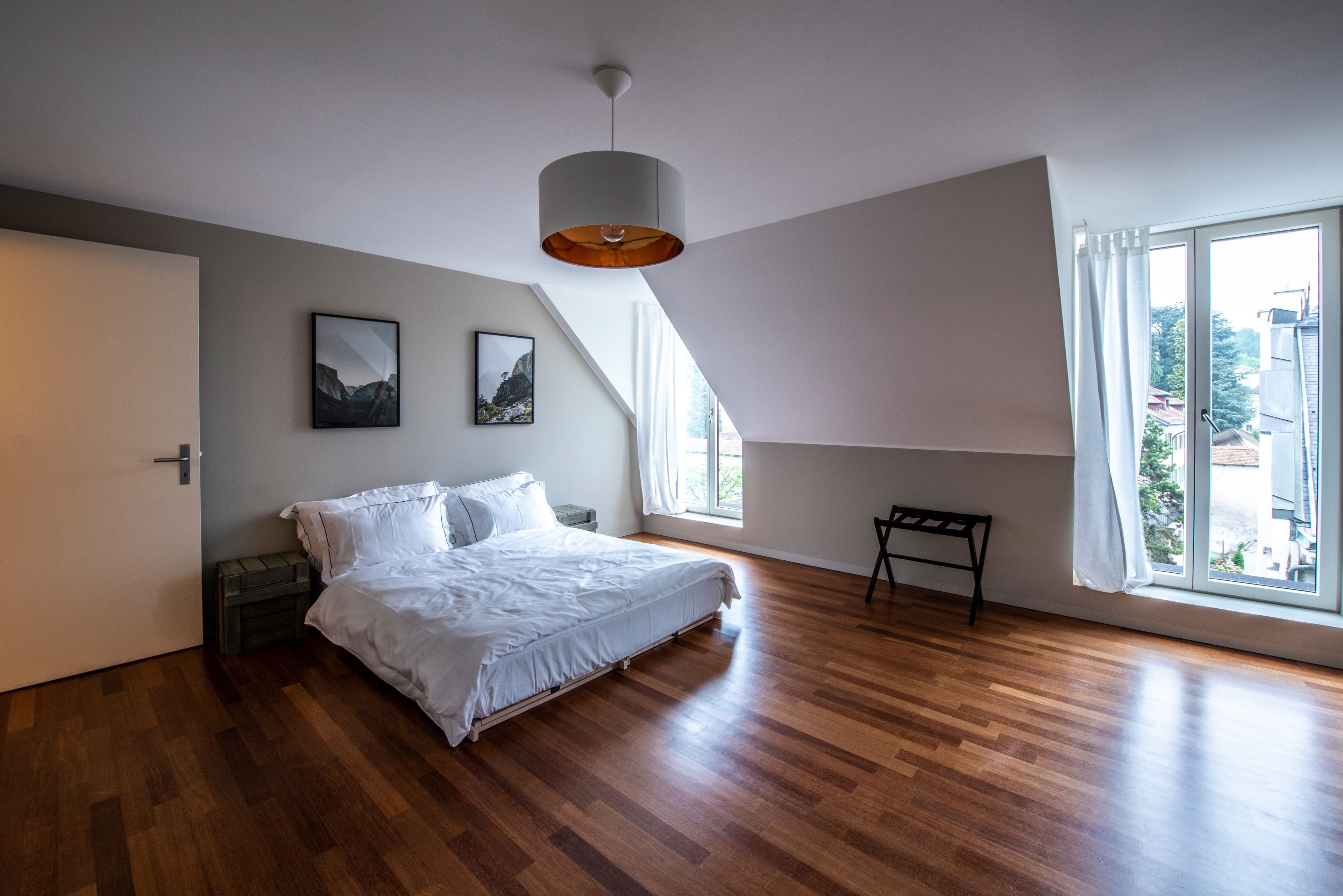 A bedroom with a large bed, a desk, and a window with curtains.