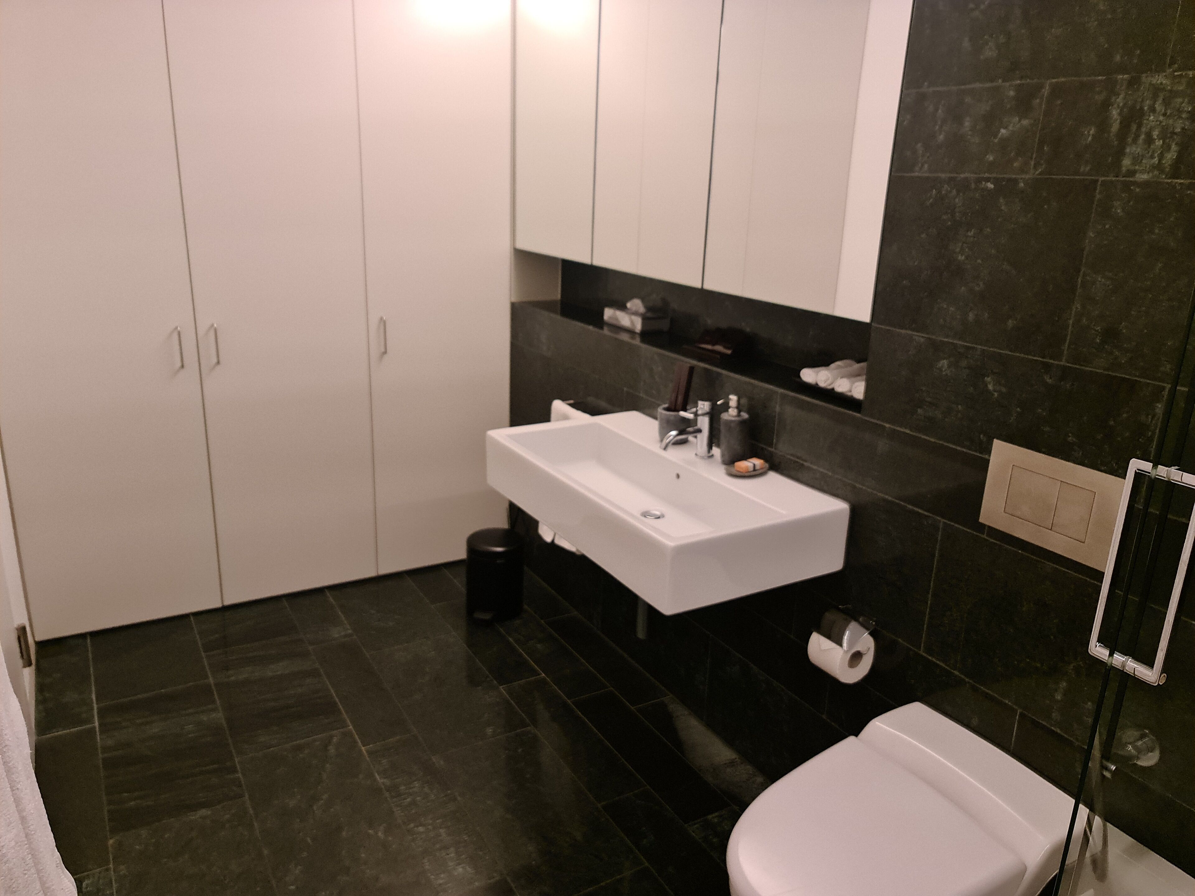 Een moderne badkamer met een witte wastafel, een donkere betegelde vloer en een wit toilet.