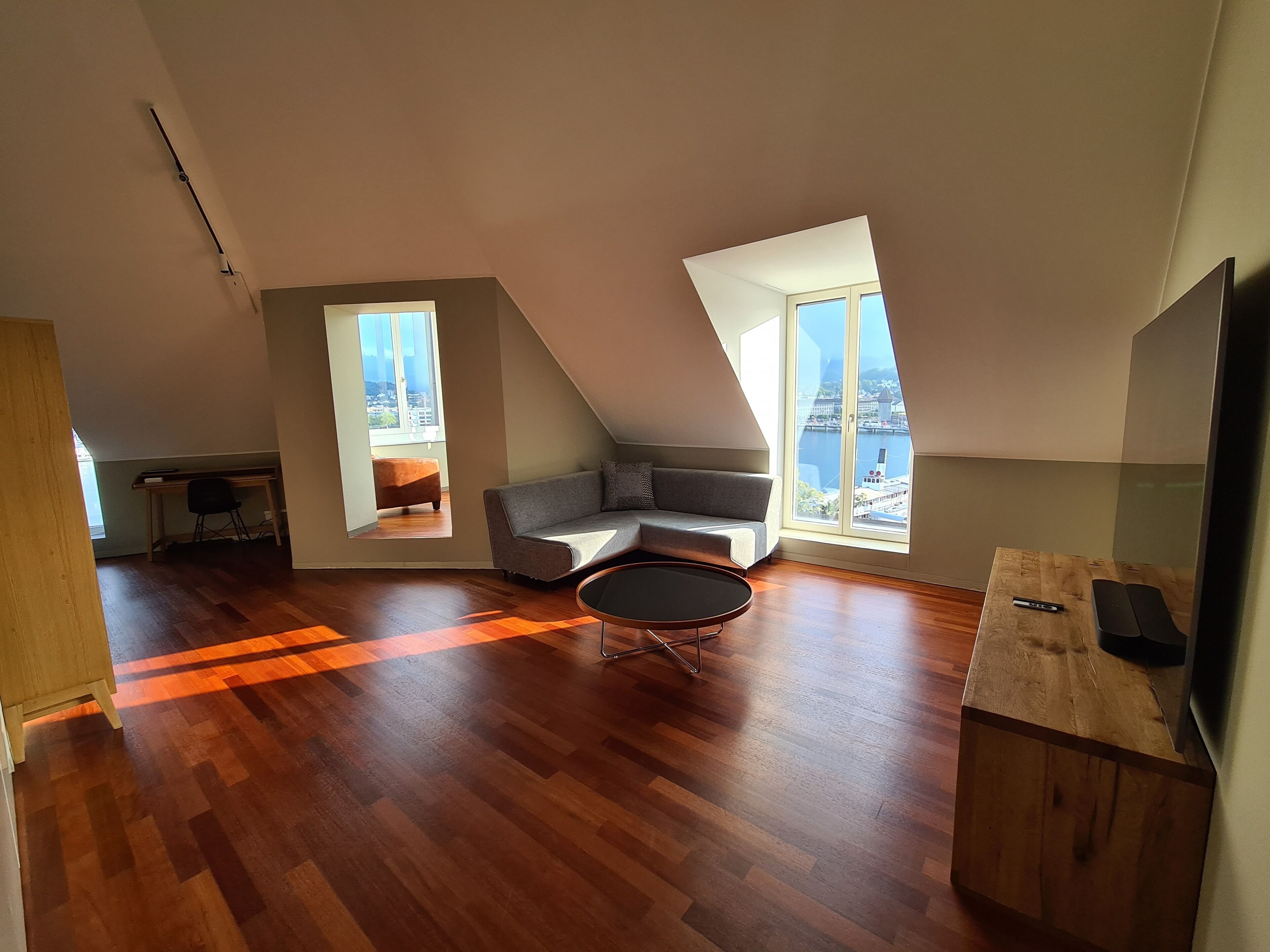 A spacious loft with a wooden floor, a gray sofa, a small round table, and a TV on a wooden stand.