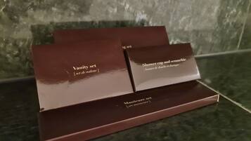 Tres cajas marrones etiquetadas 'Vanity set', 'Gorro de ducha y seruniche' y 'Set de manicura' sobre una superficie de mármol.