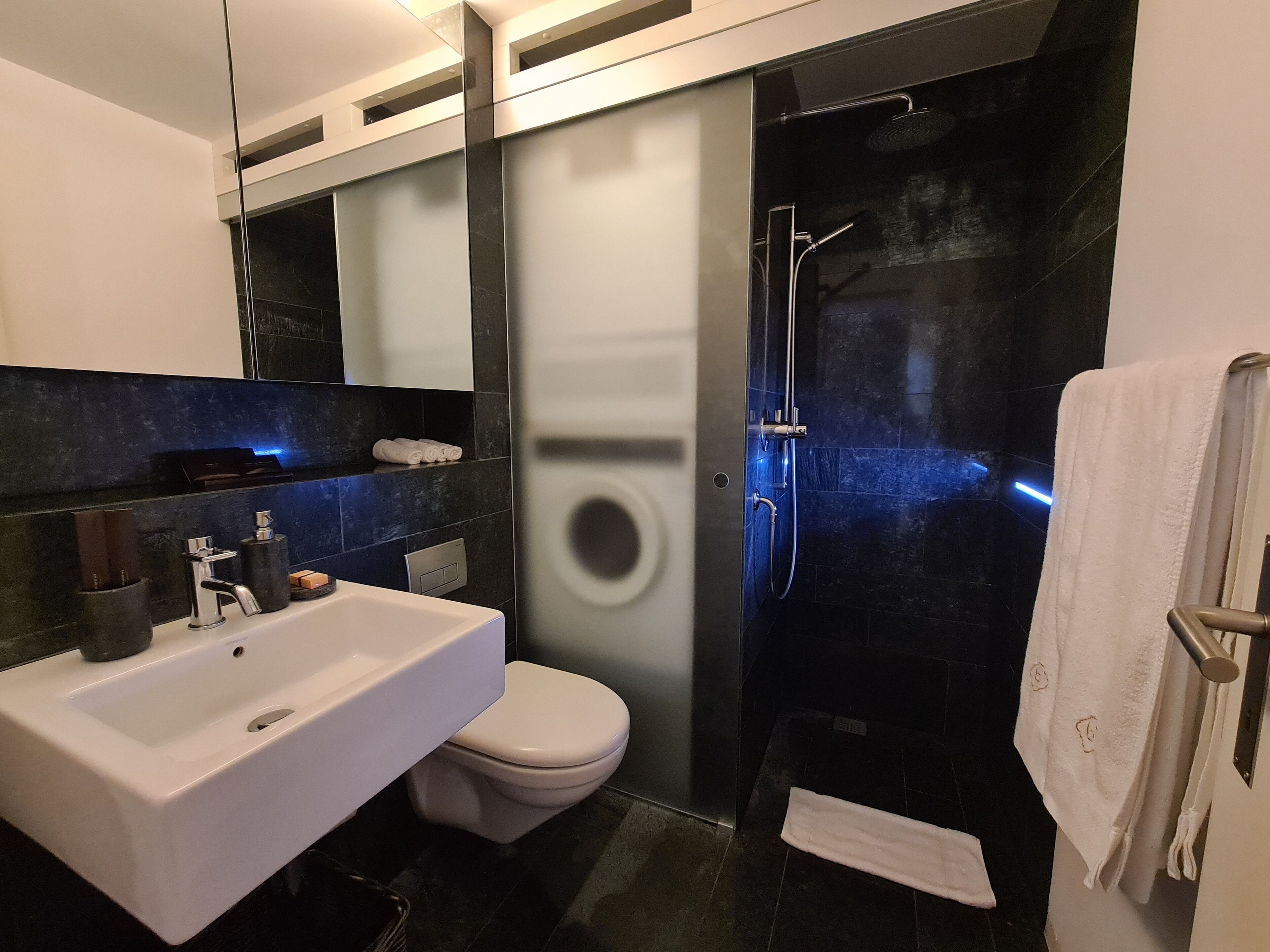 A modern bathroom with a white sink, toilet, and a glass-enclosed shower area.