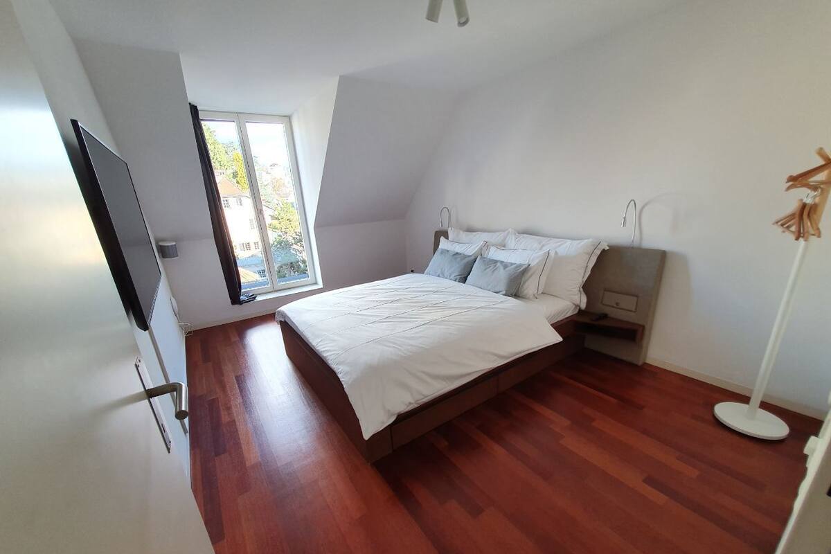 A bedroom with a bed, a bedside table, a floor lamp, and a window.