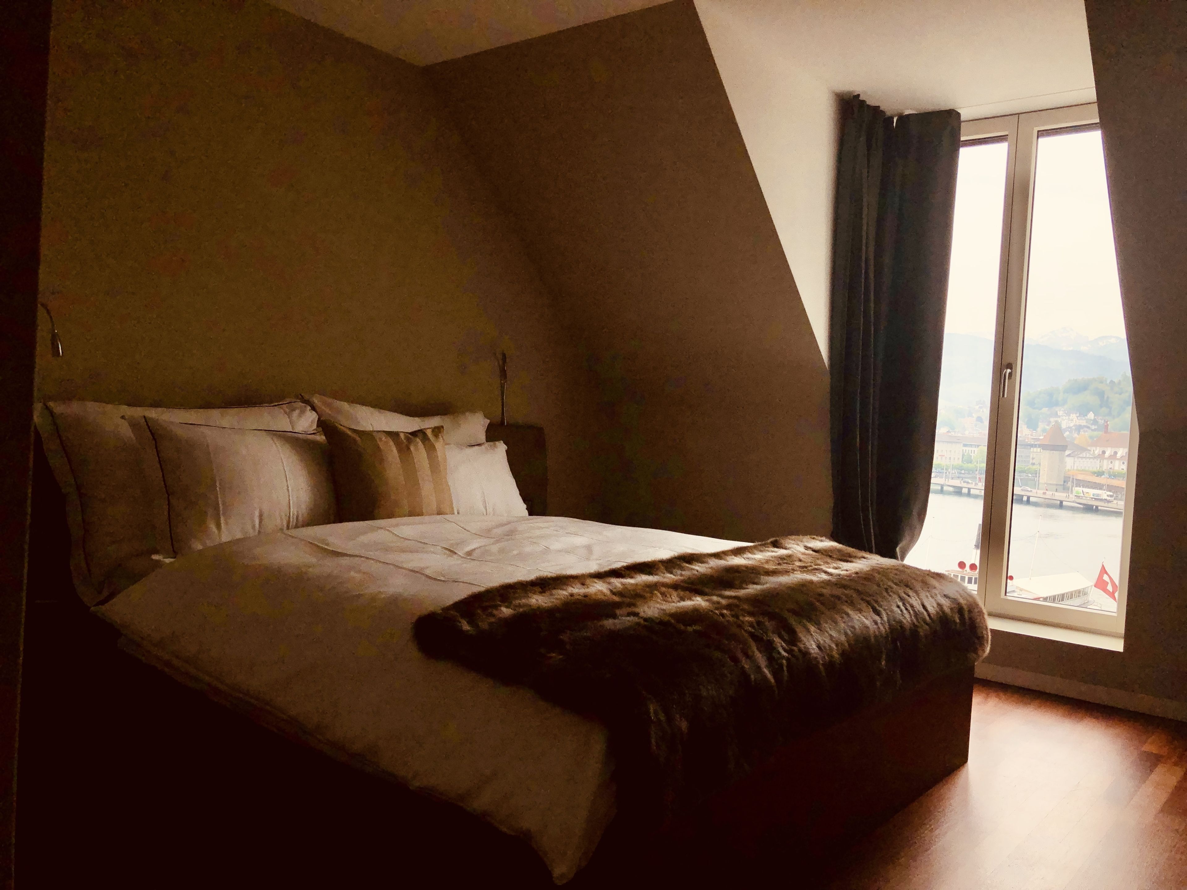 A bedroom with a large bed, a window with curtains, and a view of a cityscape.
