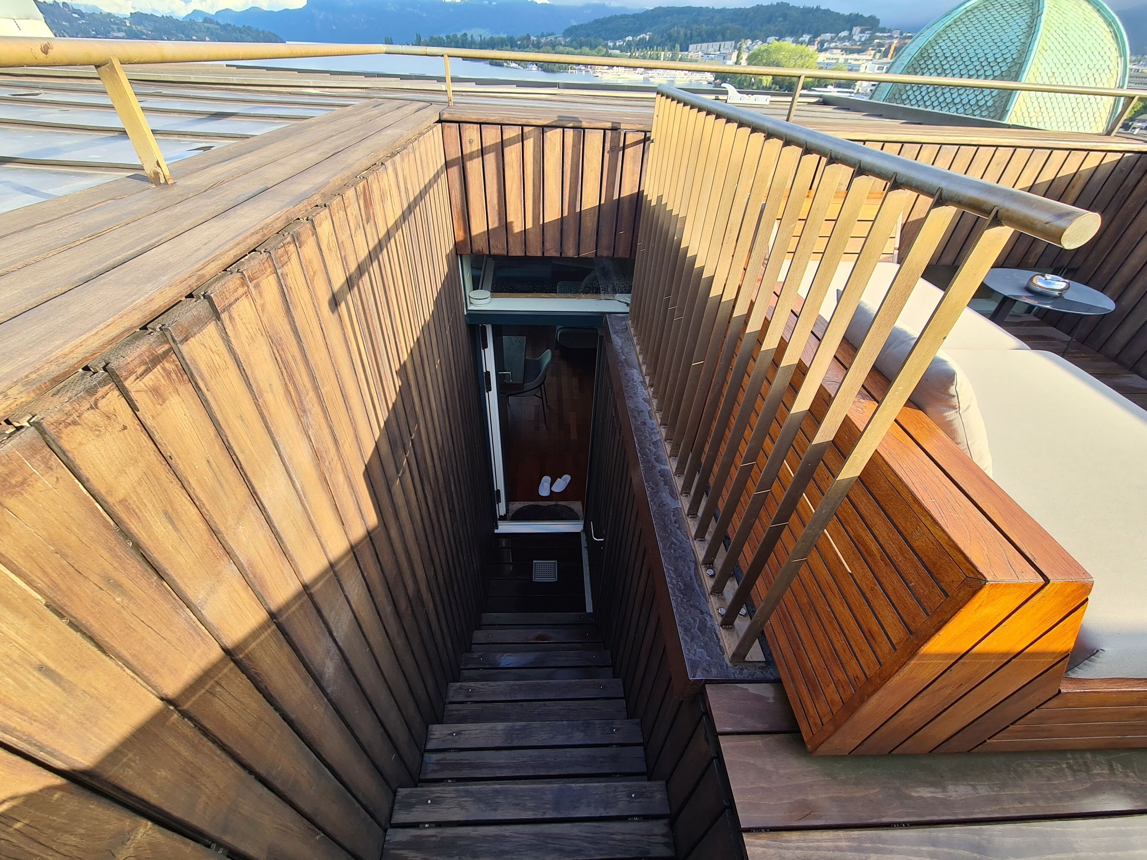 Eine Holztreppe führt zu einer Terrasse mit Blick auf eine Stadtlandschaft und Berge im Hintergrund.