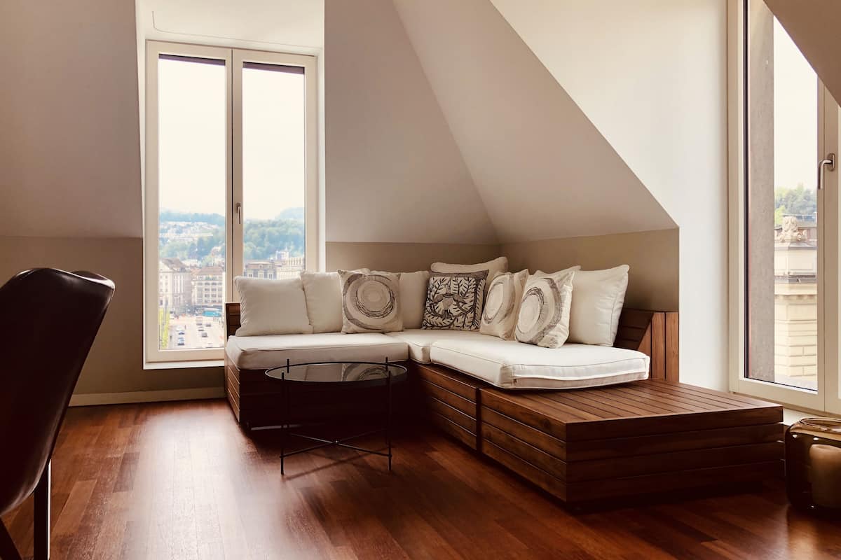 A modern loft bedroom with a built-in sofa, a wooden bench, and a large window offering a city view.