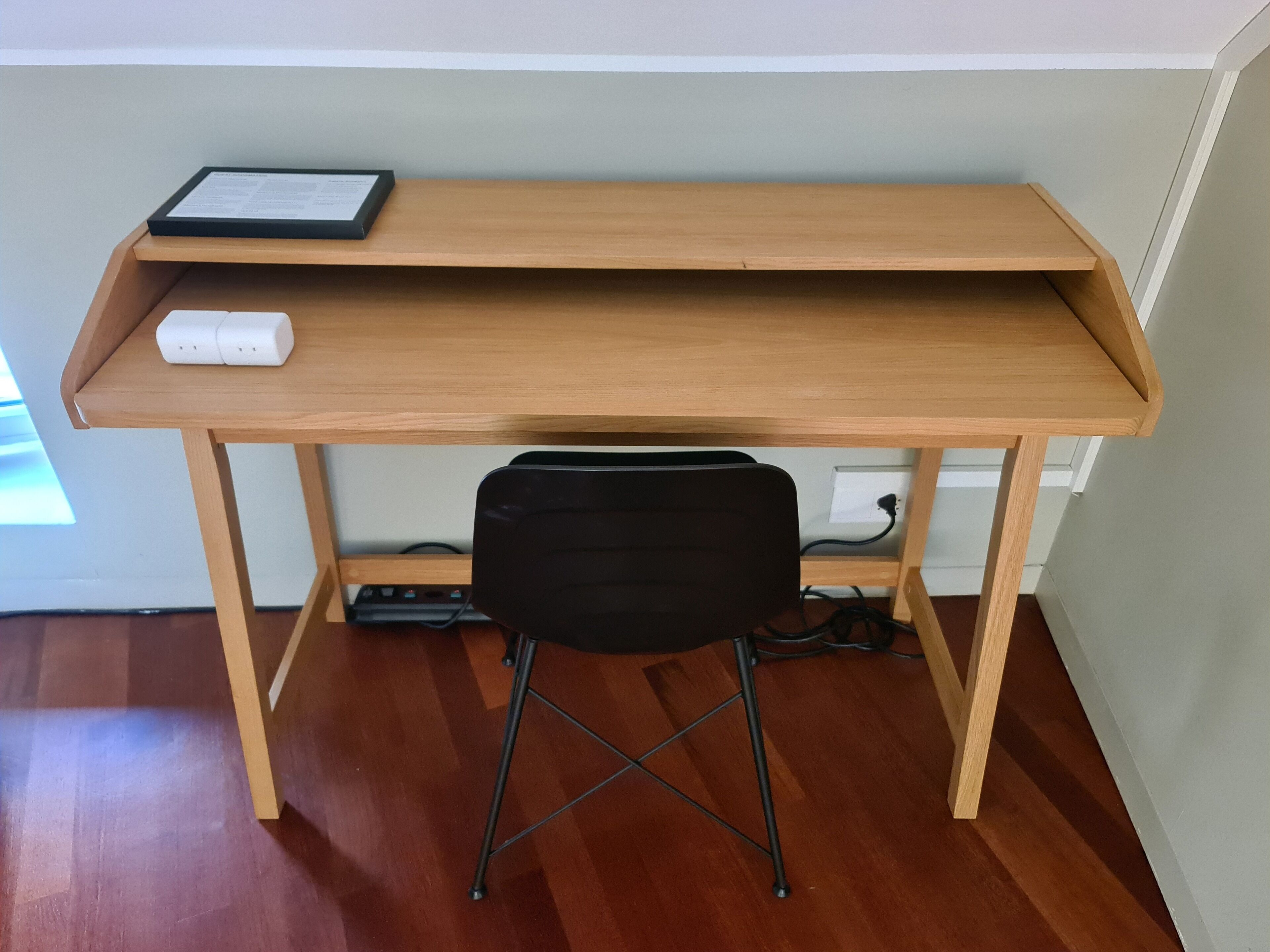 A wooden desk with a black chair, a white power strip, and a framed certificate on the desk.