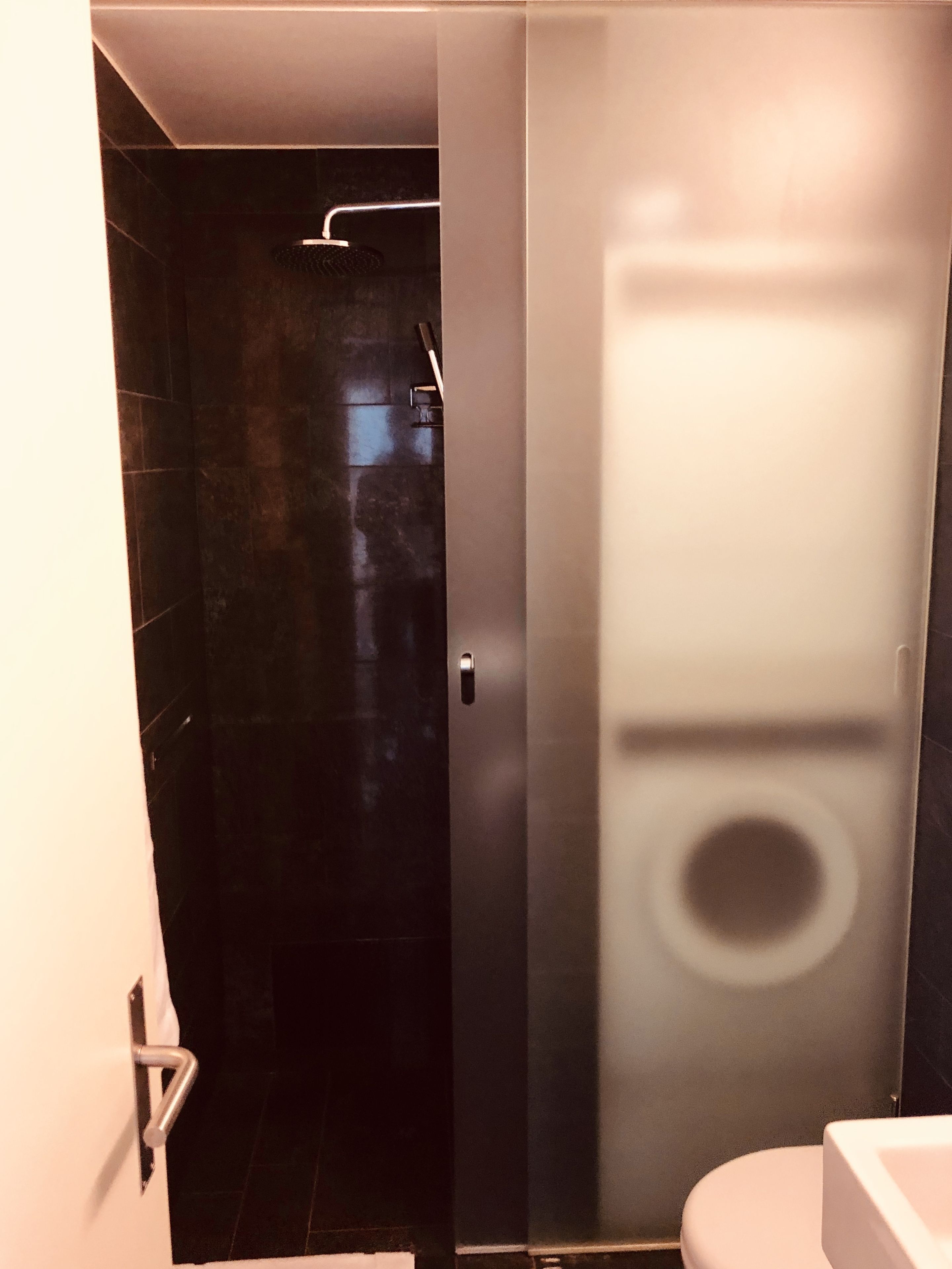 Un baño moderno con cabina de ducha de vidrio, inodoro blanco y suelo de baldosas oscuras.