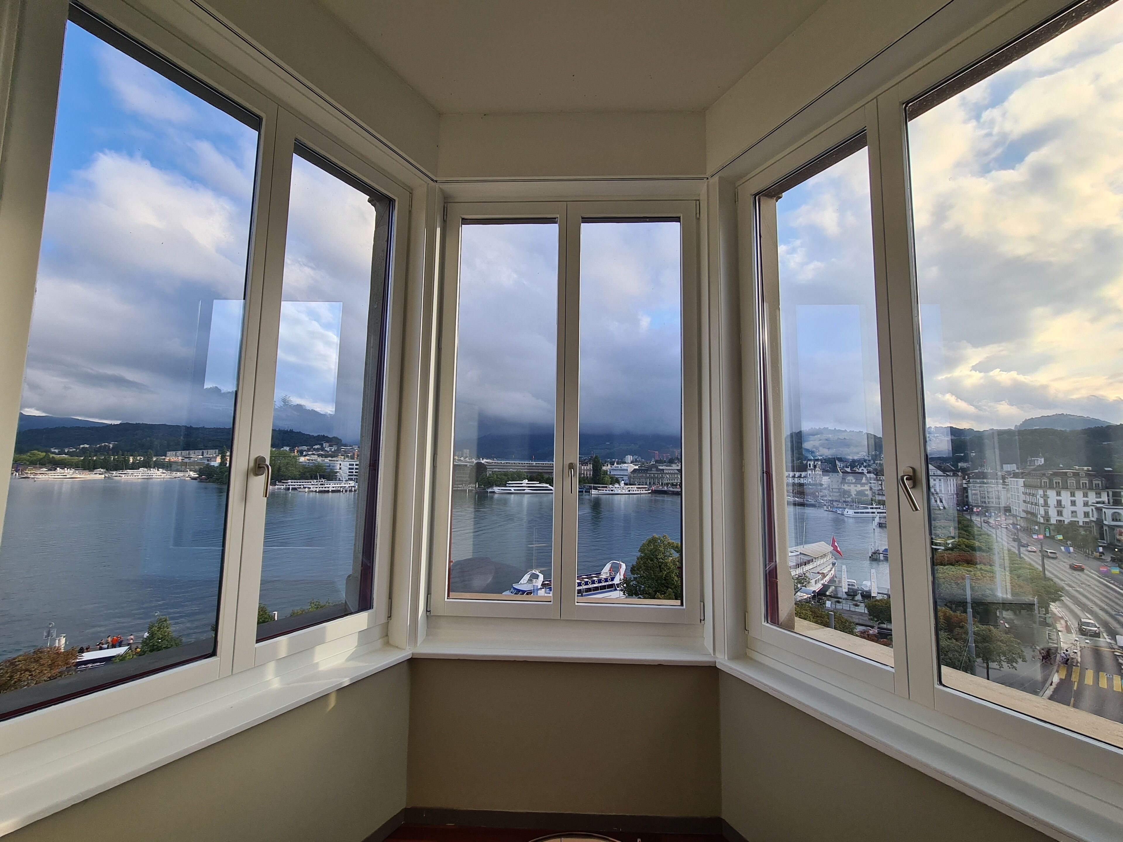 Habitación en esquina con cuatro ventanas que dan a un lago y al paisaje urbano.