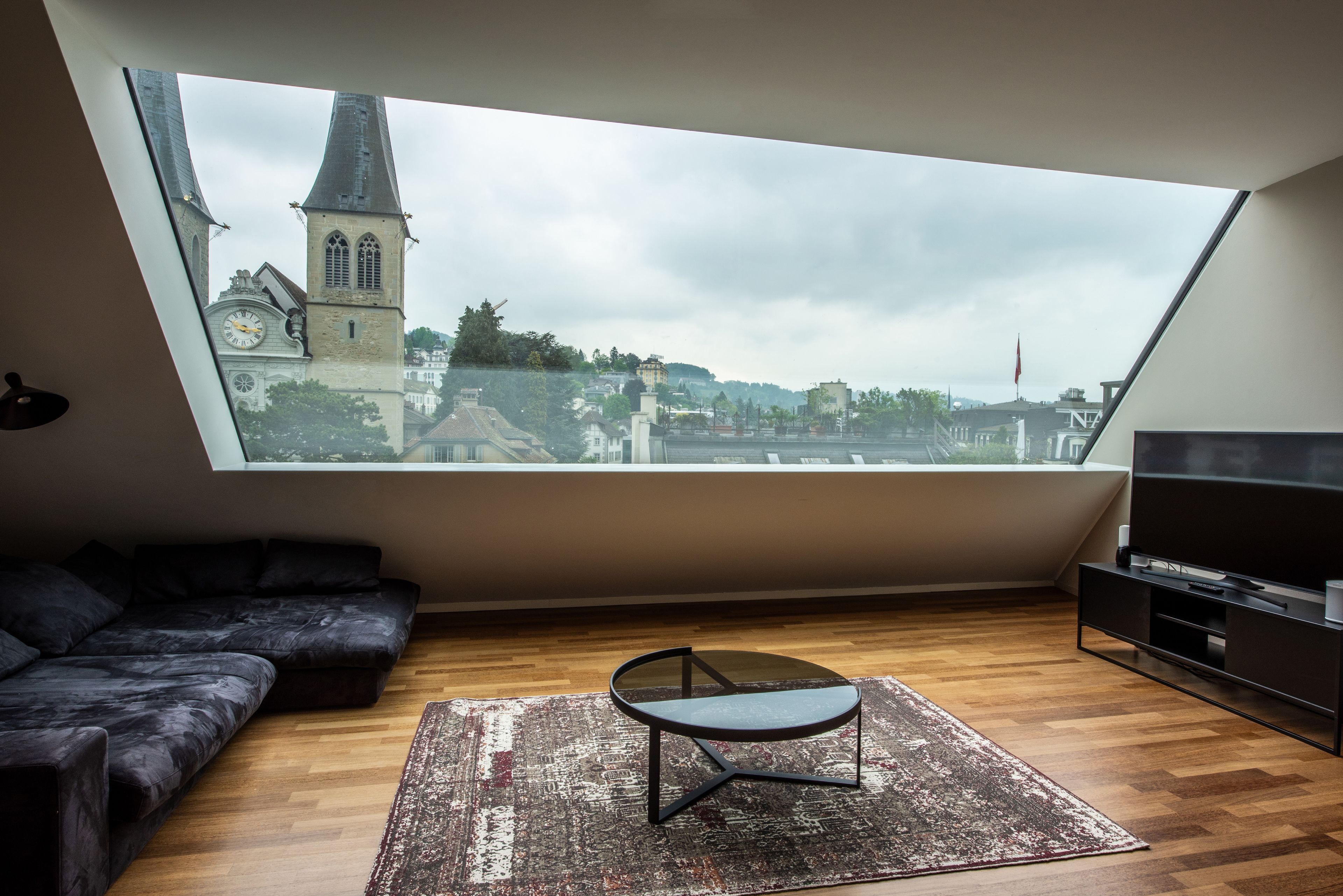 A modern loft bedroom with a skylight, a black sofa, a small table, and a TV.