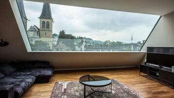A modern loft bedroom with a skylight, a black sofa, a small table, and a TV.