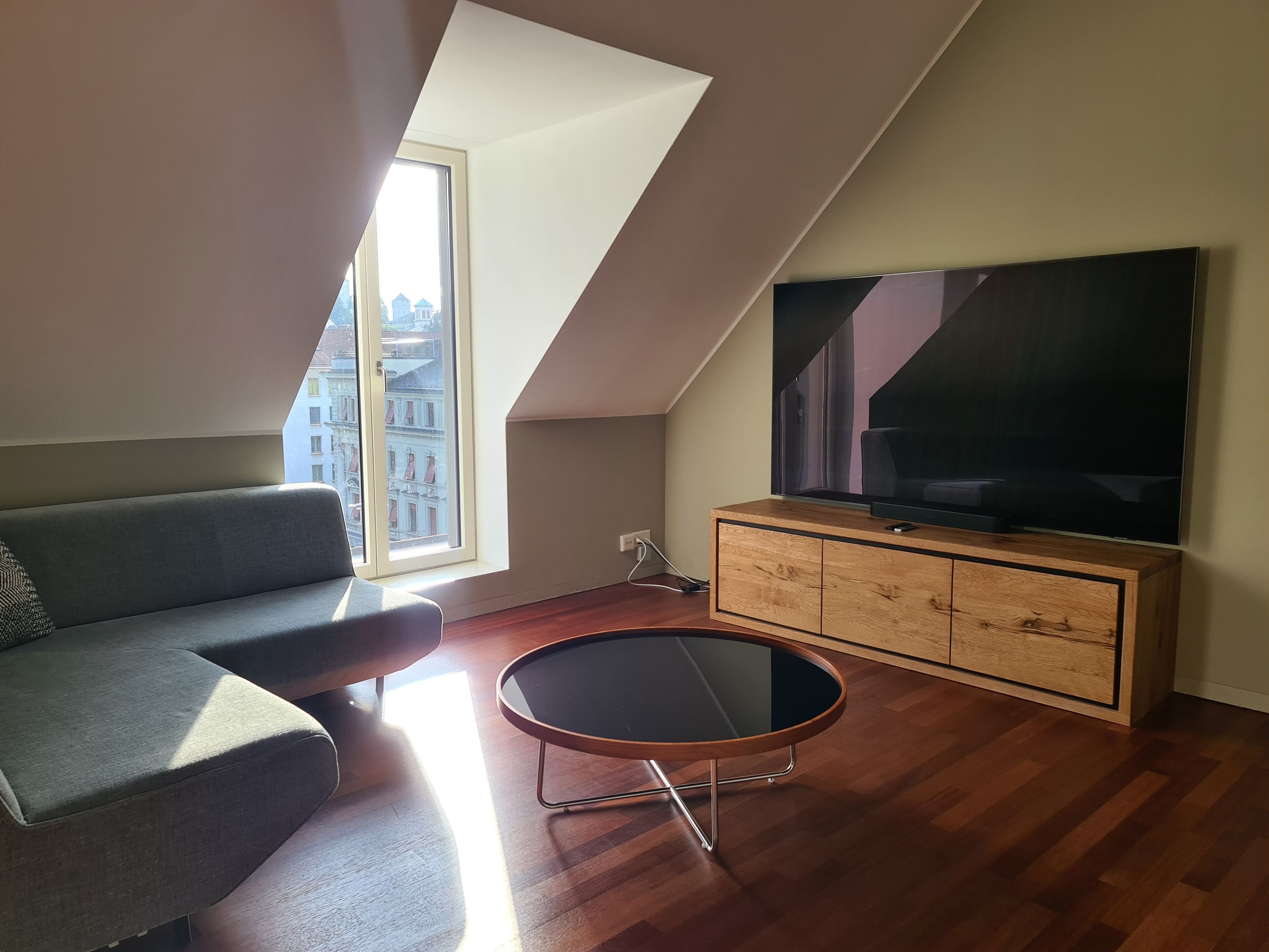Un salon moderne avec un plafond de style industriel, un grand téléviseur à écran plat, un canapé gris et un meuble en bois.