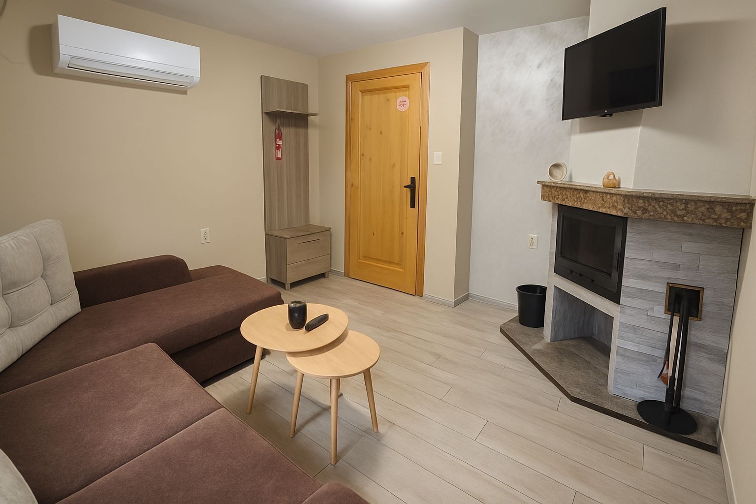A living room with a sofa, a small round table with a remote, a fireplace, and a television mounted on the wall.