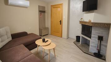 A living room with a sofa, a small round table with a remote, a fireplace, and a television mounted on the wall.