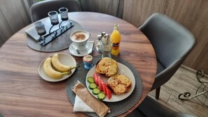 Una mesa redonda con un plato de comida, una taza de café, una botella de jugo y un pequeño recipiente de azúcar.