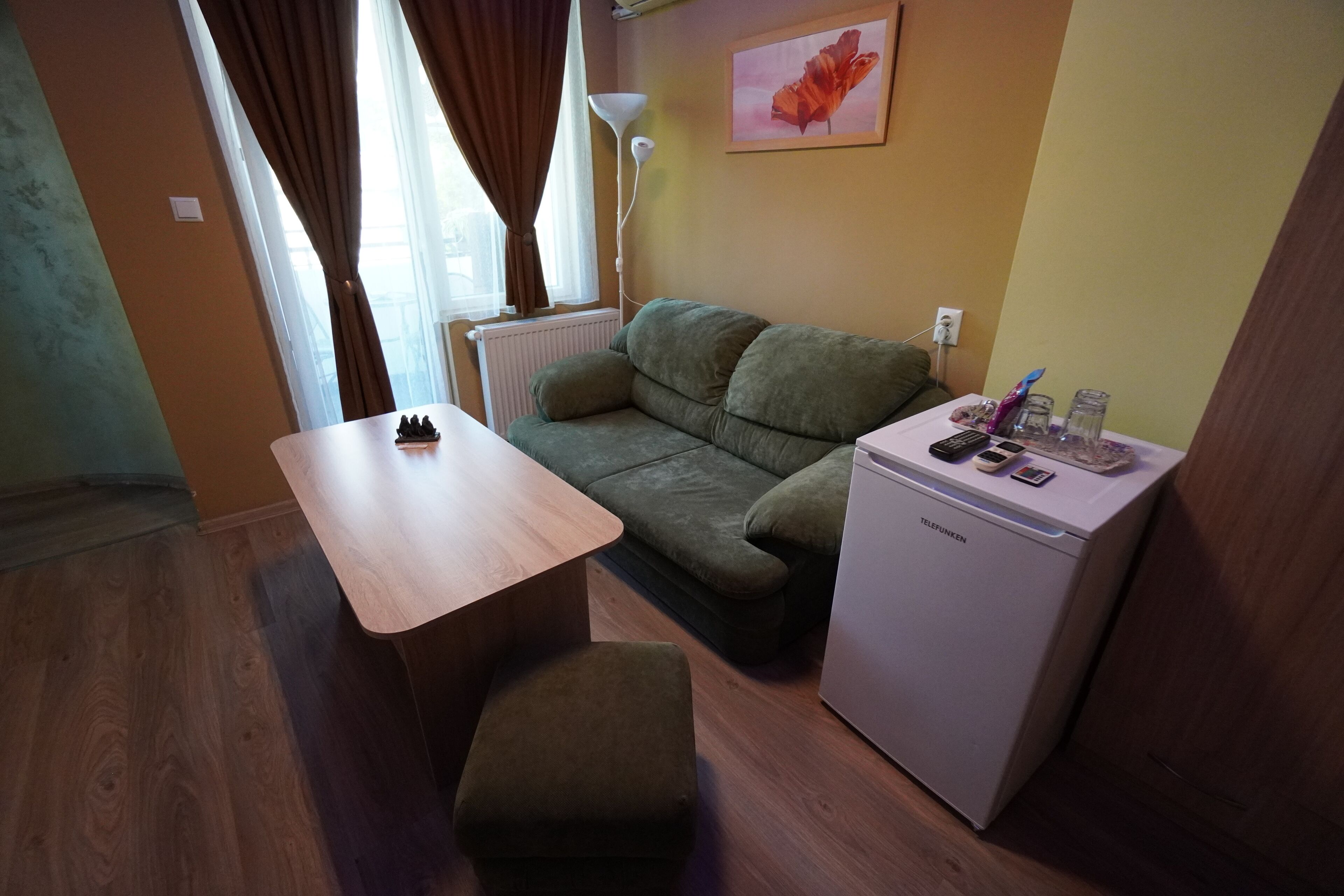 Um espaço compacto com sofá, uma mesinha, frigorífico e uma lâmpada.