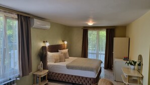 Un dormitorio con cama, lámparas de noche, aire acondicionado, una mesita, una silla y un refrigerador.