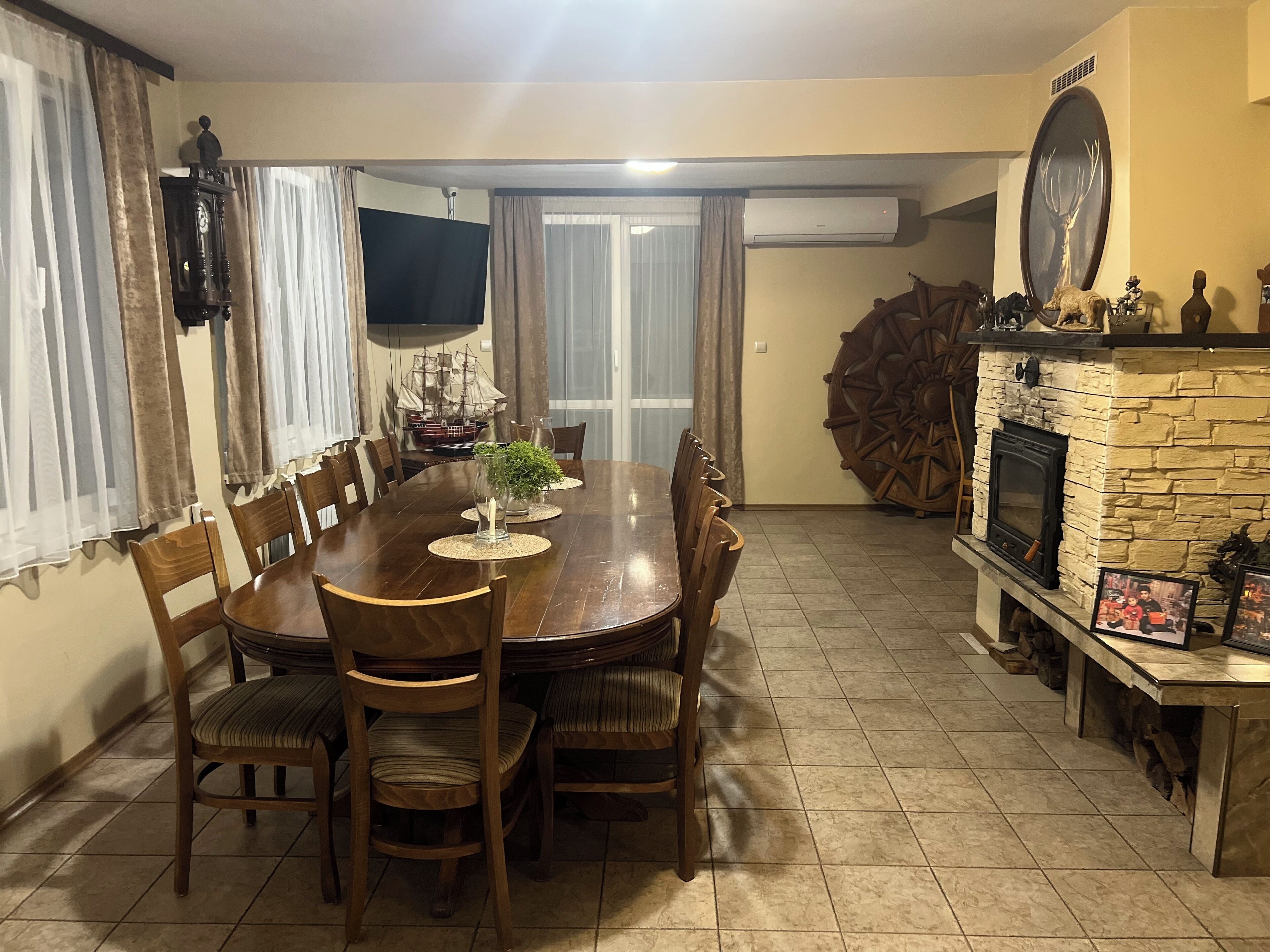 Un comedor con una gran mesa de madera, sillas, un televisor, un modelo de barco y una chimenea de piedra.