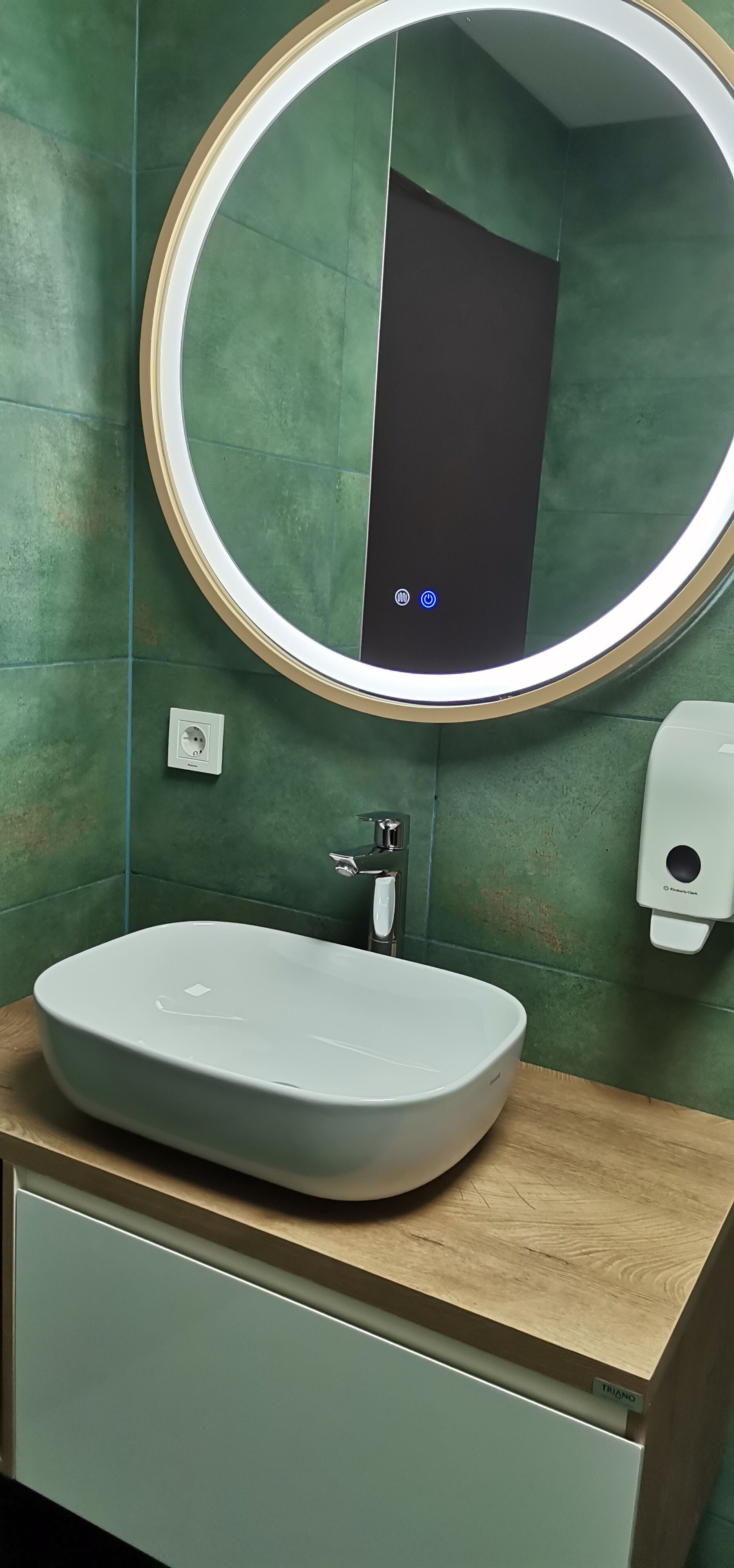 A bathroom with a round mirror, a white sink, and a wooden countertop.