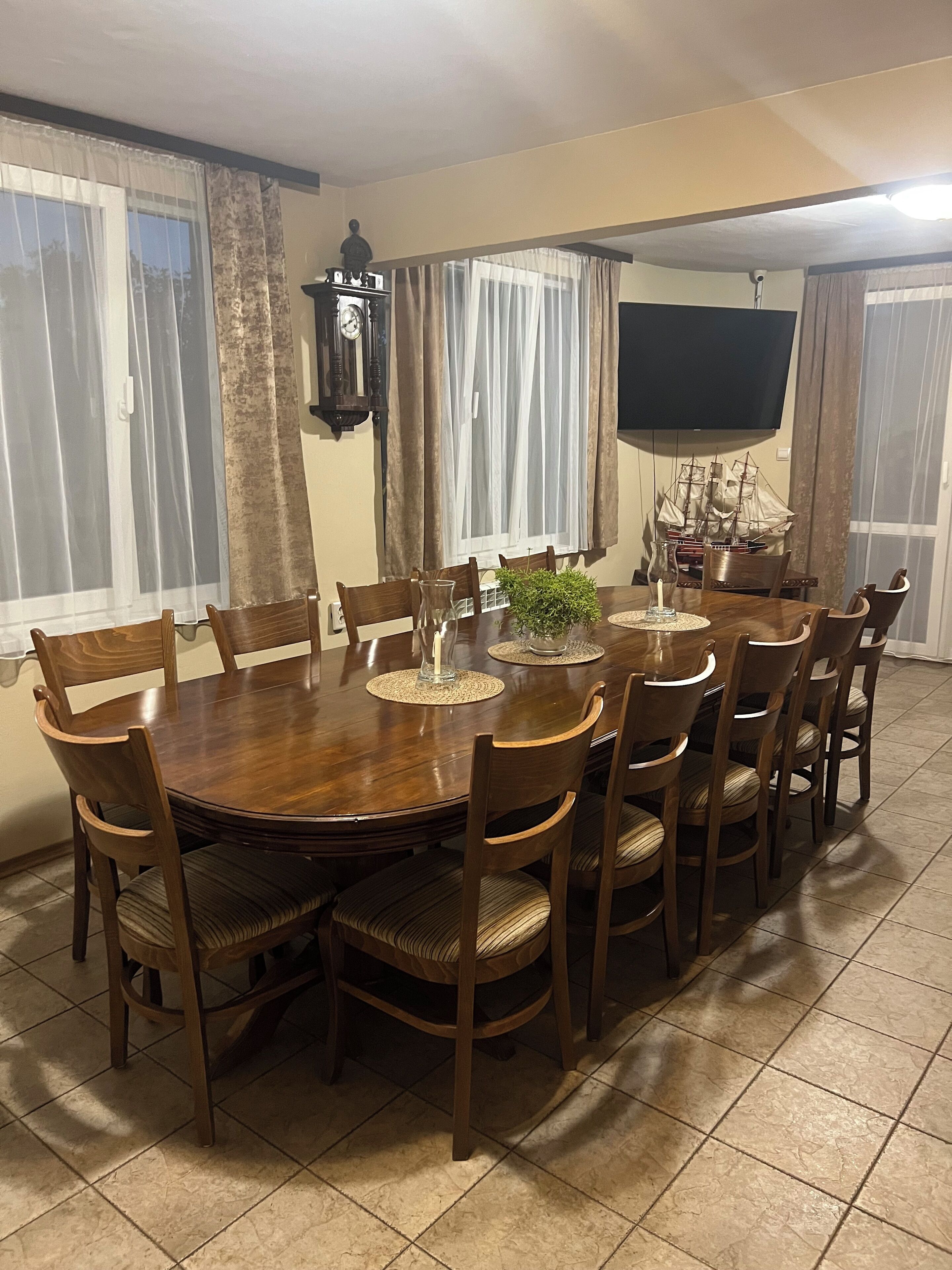 A dining room with a round wooden table, eight chairs, a television, and curtains.