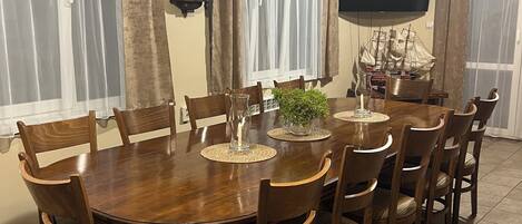 A dining room with a round wooden table, eight chairs, a television, and curtains.
