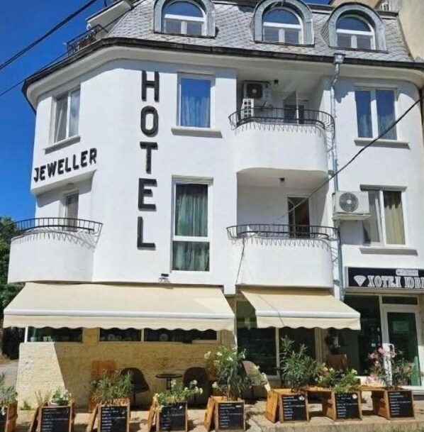 A hotel with a prominent 'HOTEL' sign on the facade, a balcony, and outdoor seating with plants. - Hotel Jeweller (Ruse)