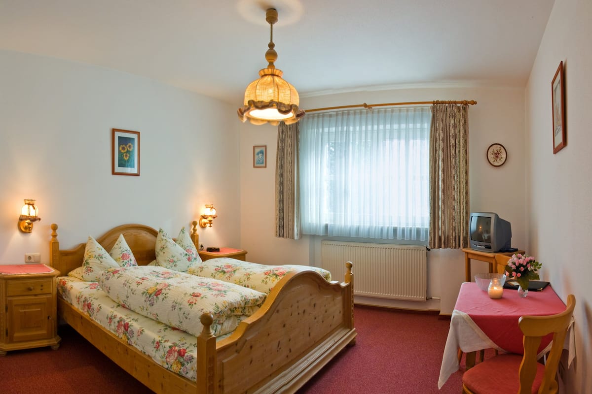 Un dormitorio con una cama de madera, un escritorio con silla, un televisor y una ventana con cortinas.