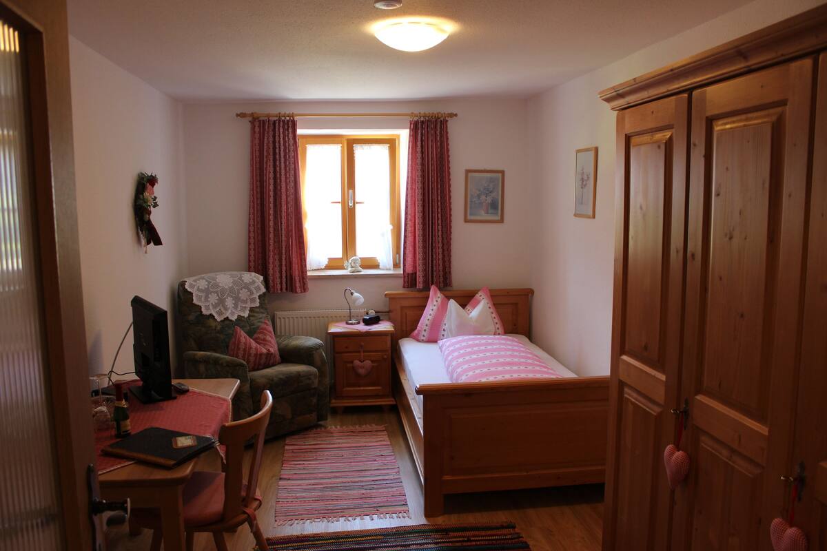 Un dormitorio con una cama de madera, un escritorio con computadora, una silla, una ventana con cortinas y un armario.